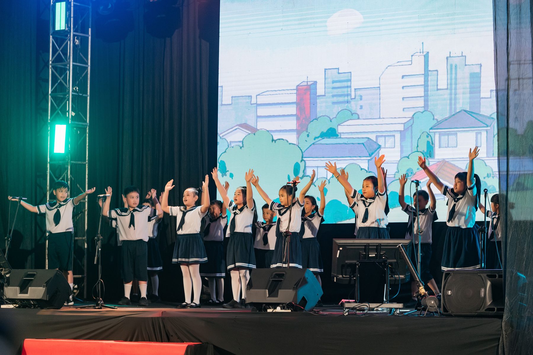 Primary students singing on stage with their arms raised