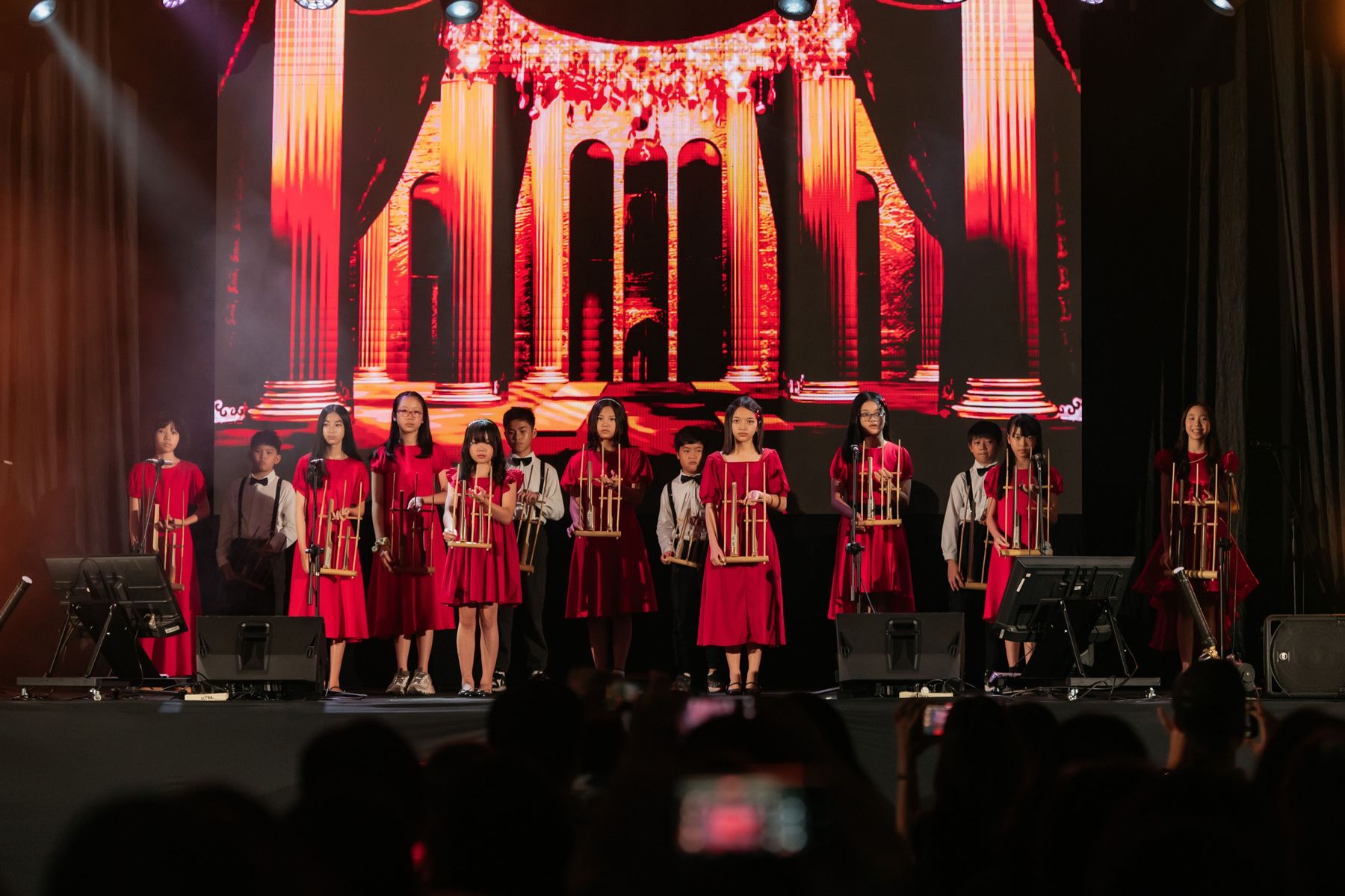 Students in red costumes performing angklung on stage